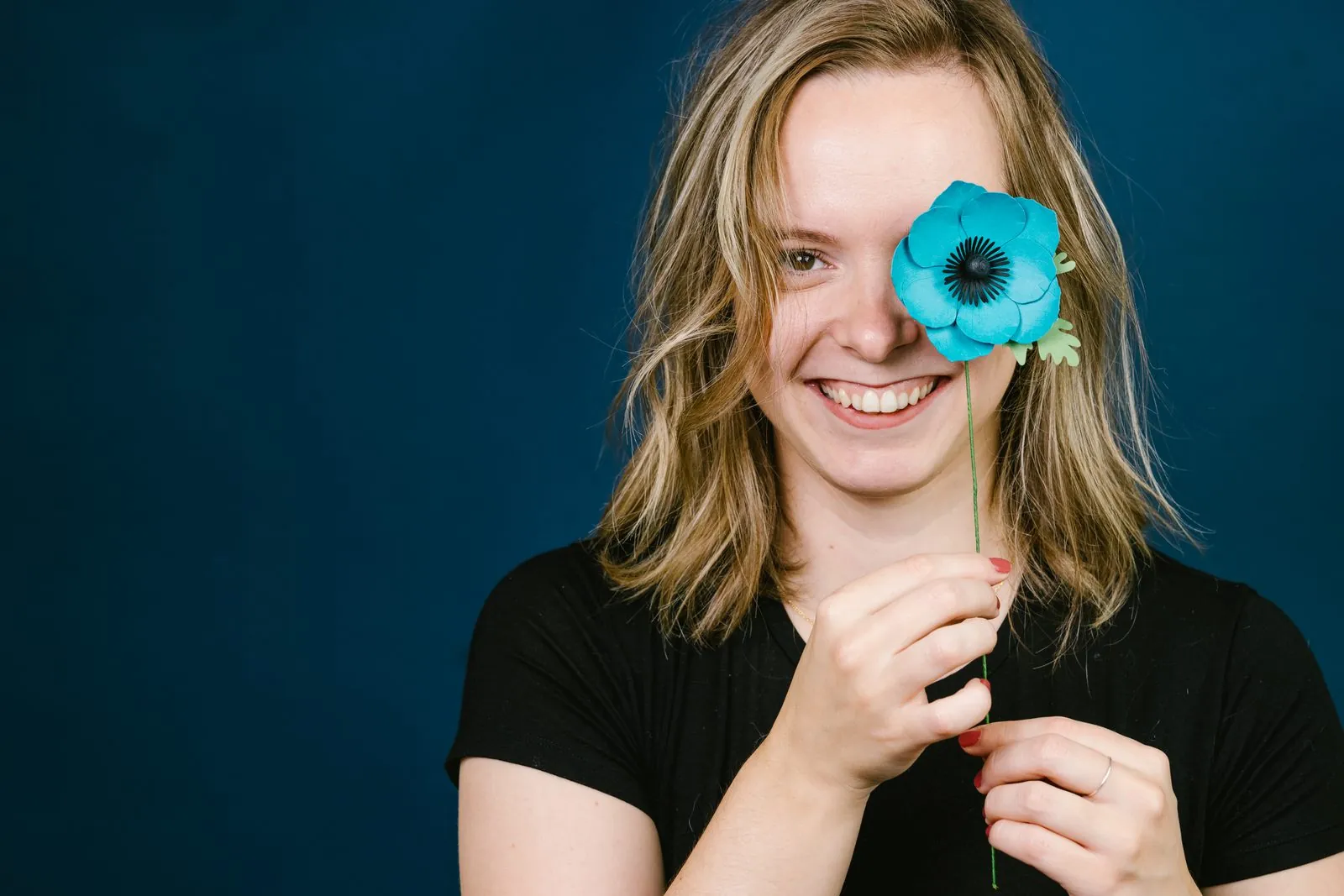 Oriane ABT, artisane créatrice de fleurs en papier, une anémone bleue en papier devant l'œil